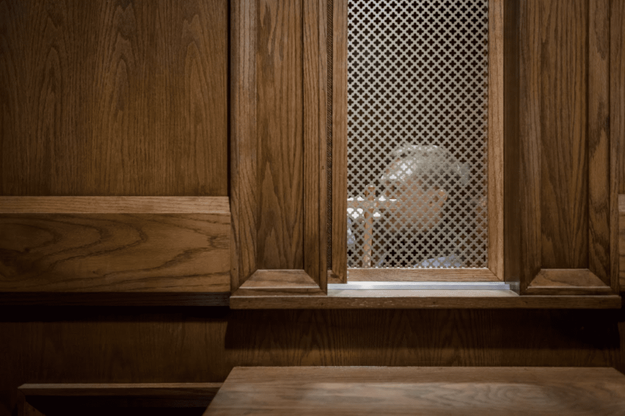 A priest waits behind a screen in a church.